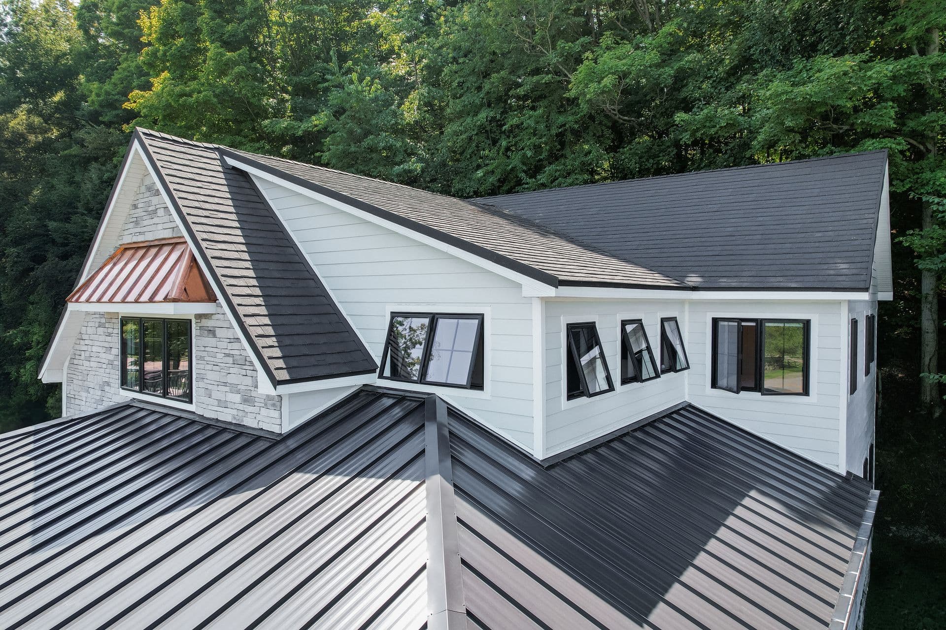A modern white house with contrasting black roofs and windows, nestled among dense green trees.