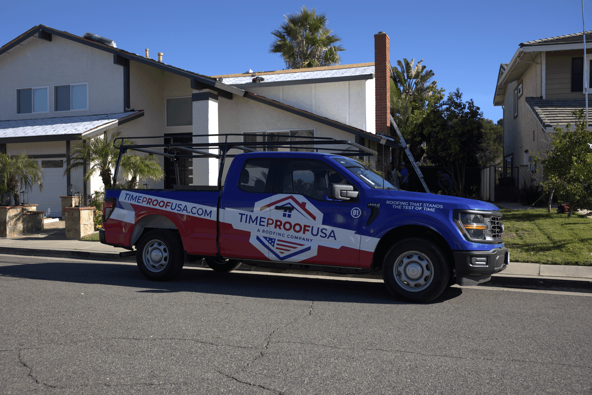 A blue and red TimeProofUSA branded pickup truck parked on a residential street in front of a house undergoing roofing work.