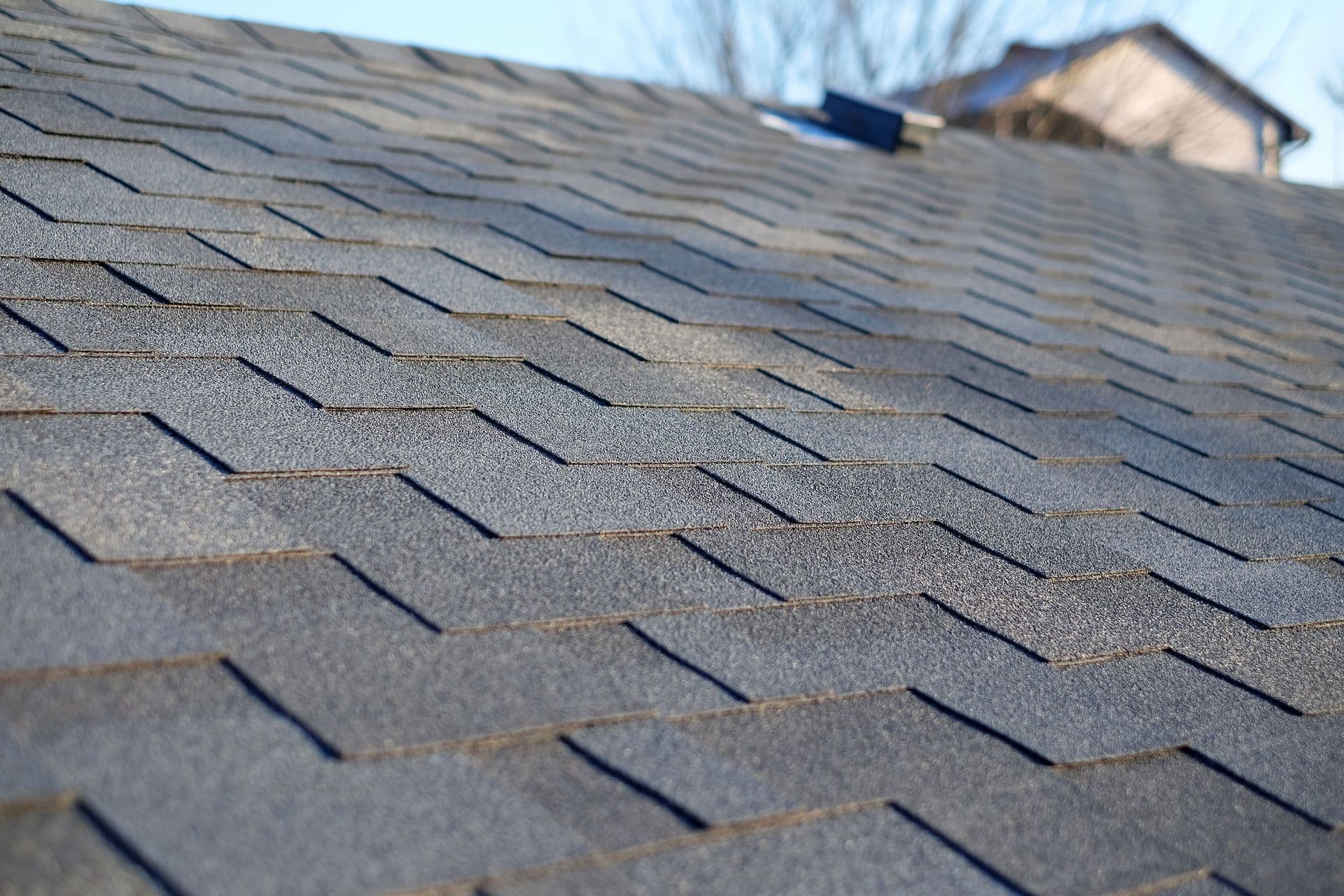 Close-up of a gray asphalt shingle roof with a textured, overlapping pattern under bright sunlight.