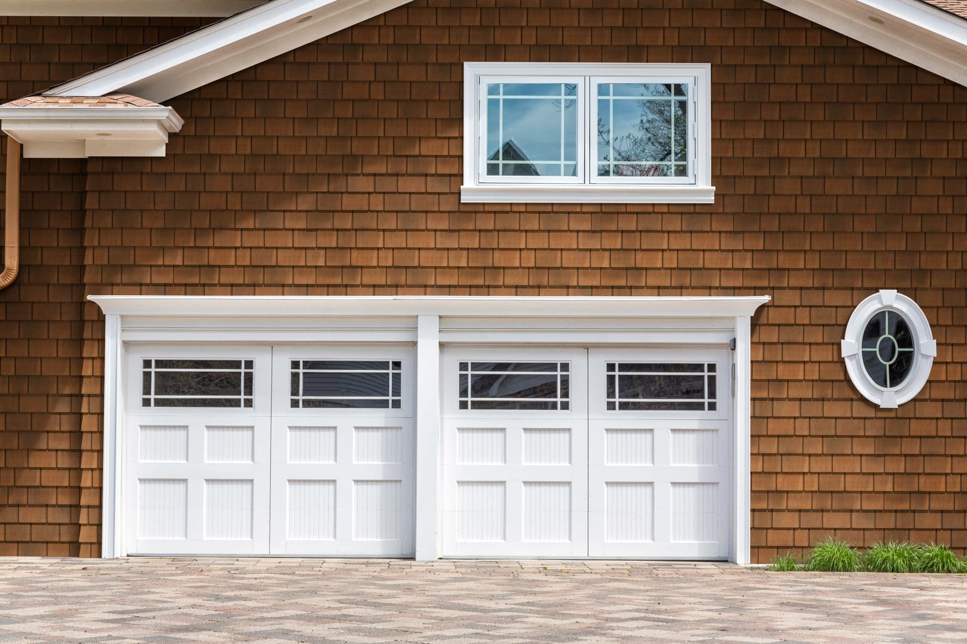 Two white garage doors with glass panels set into a brown shingled house facade.