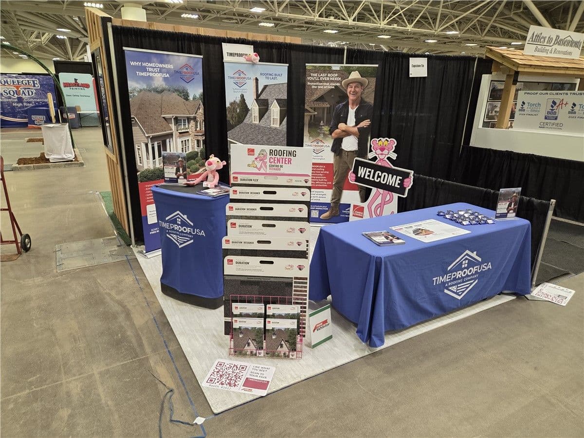 A blue-themed trade show booth for TimeProofUSA showcasing roofing products, promotional materials, and a pink Panther mascot.