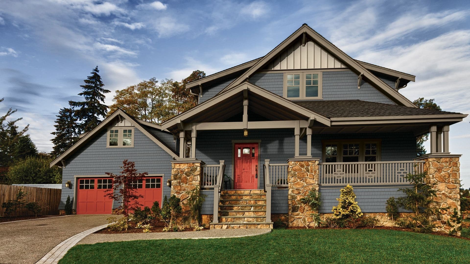 A modern blue house with a red front door and stone accents under a partly cloudy sky.