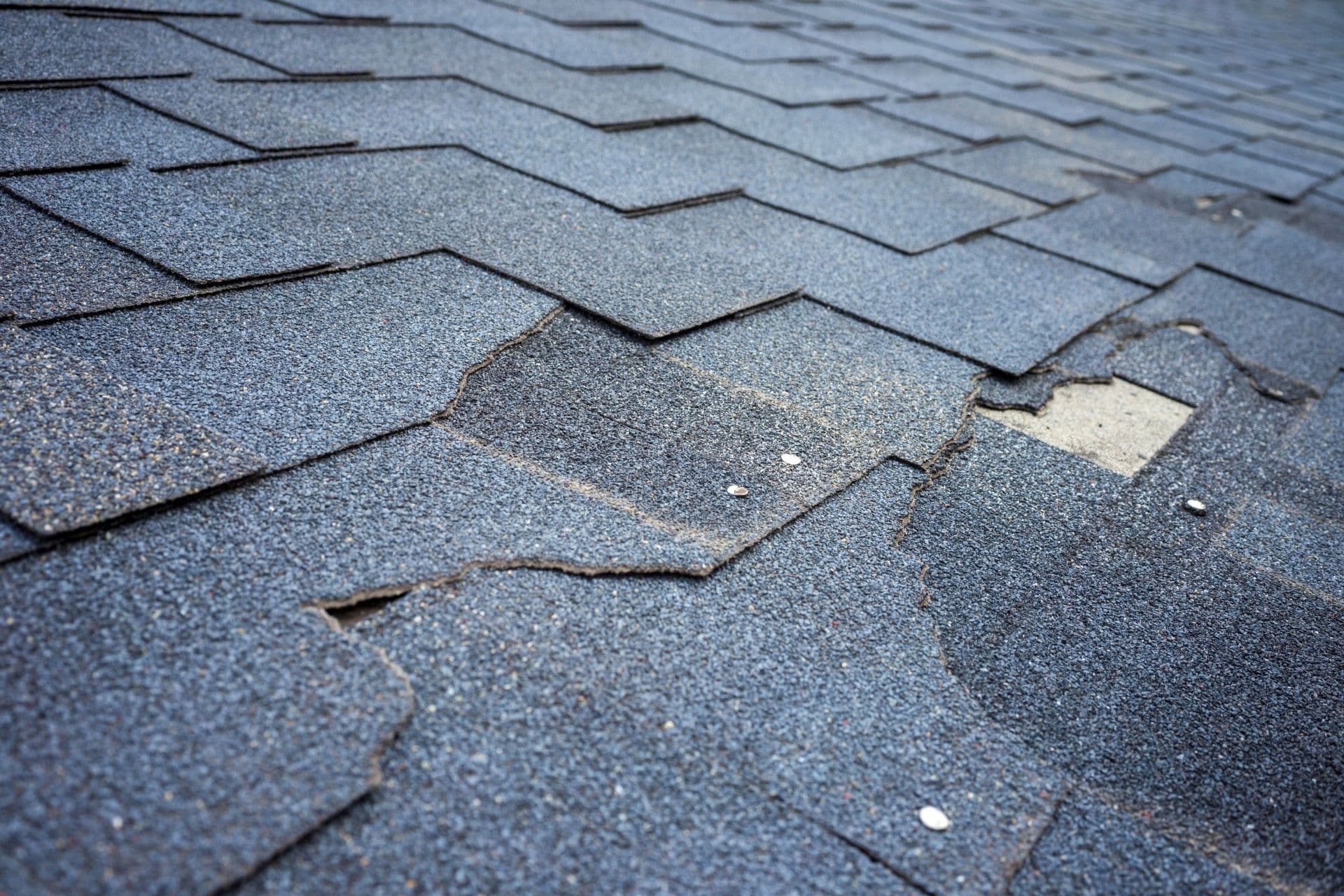 Close-up of weathered, cracked asphalt shingles with visible wear and exposed underlayment.
