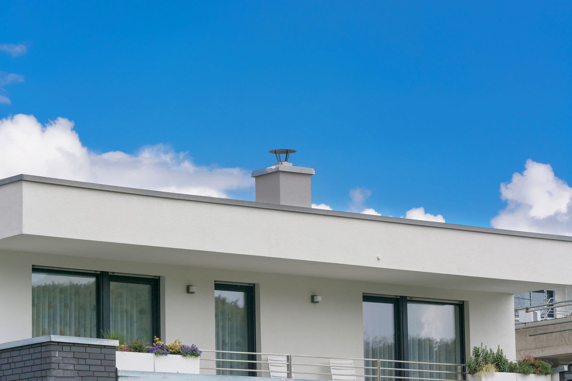 A modern white house with large windows and a balcony under a bright blue sky with scattered clouds.