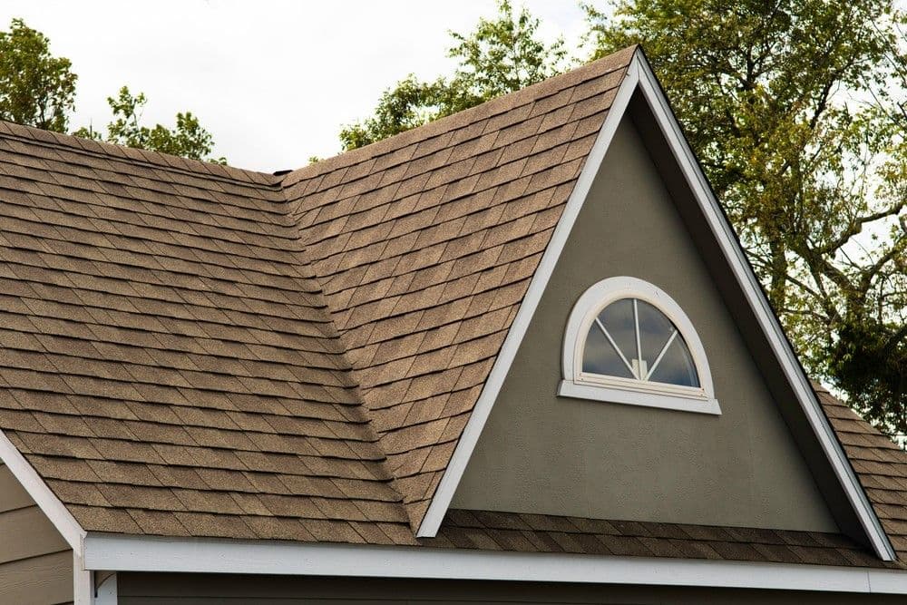 A close-up of a brown shingle roof with a white-trimmed arched window on a gable end.