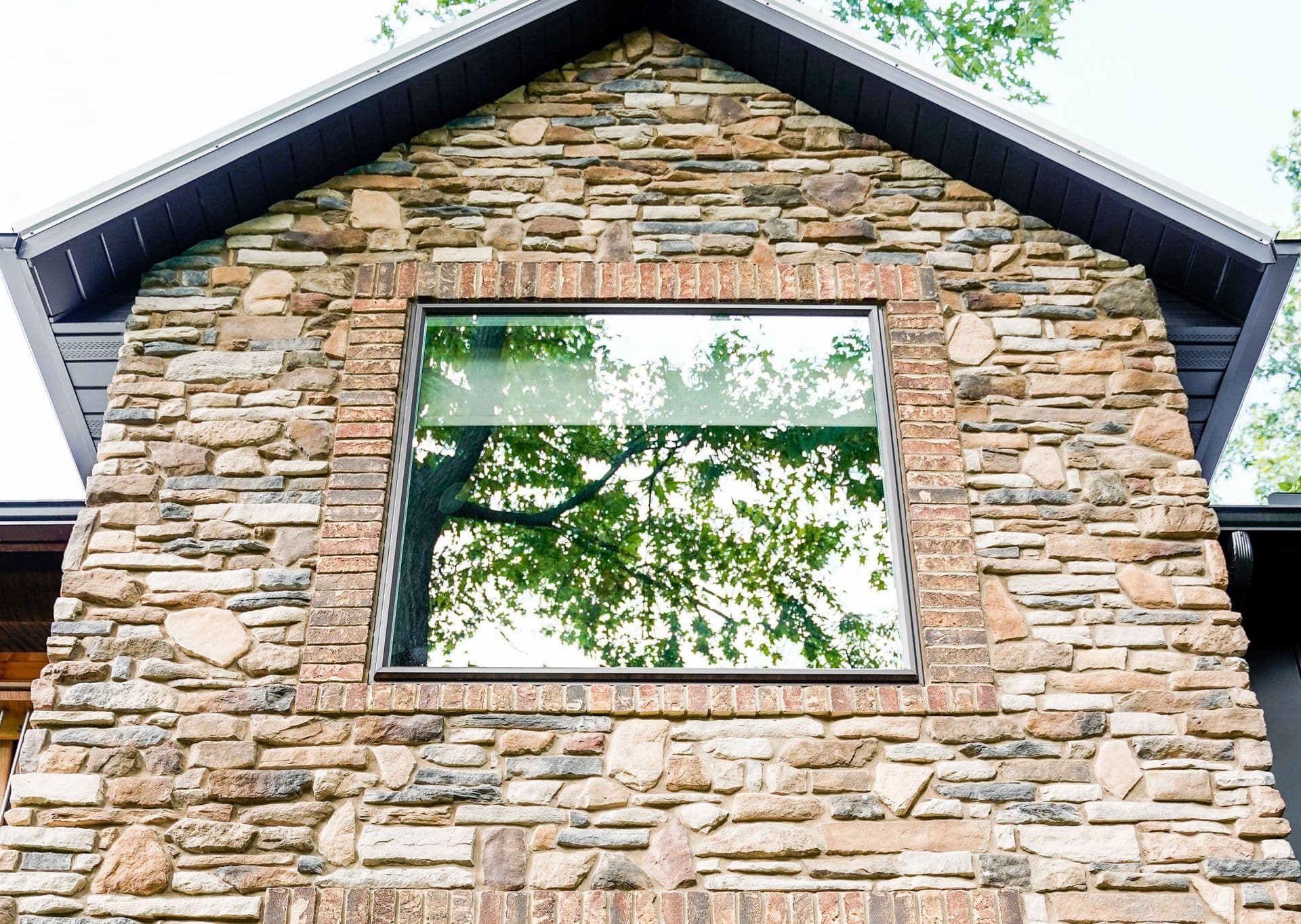 A modern window framed in brick set into a rustic stone wall under a dark roof.