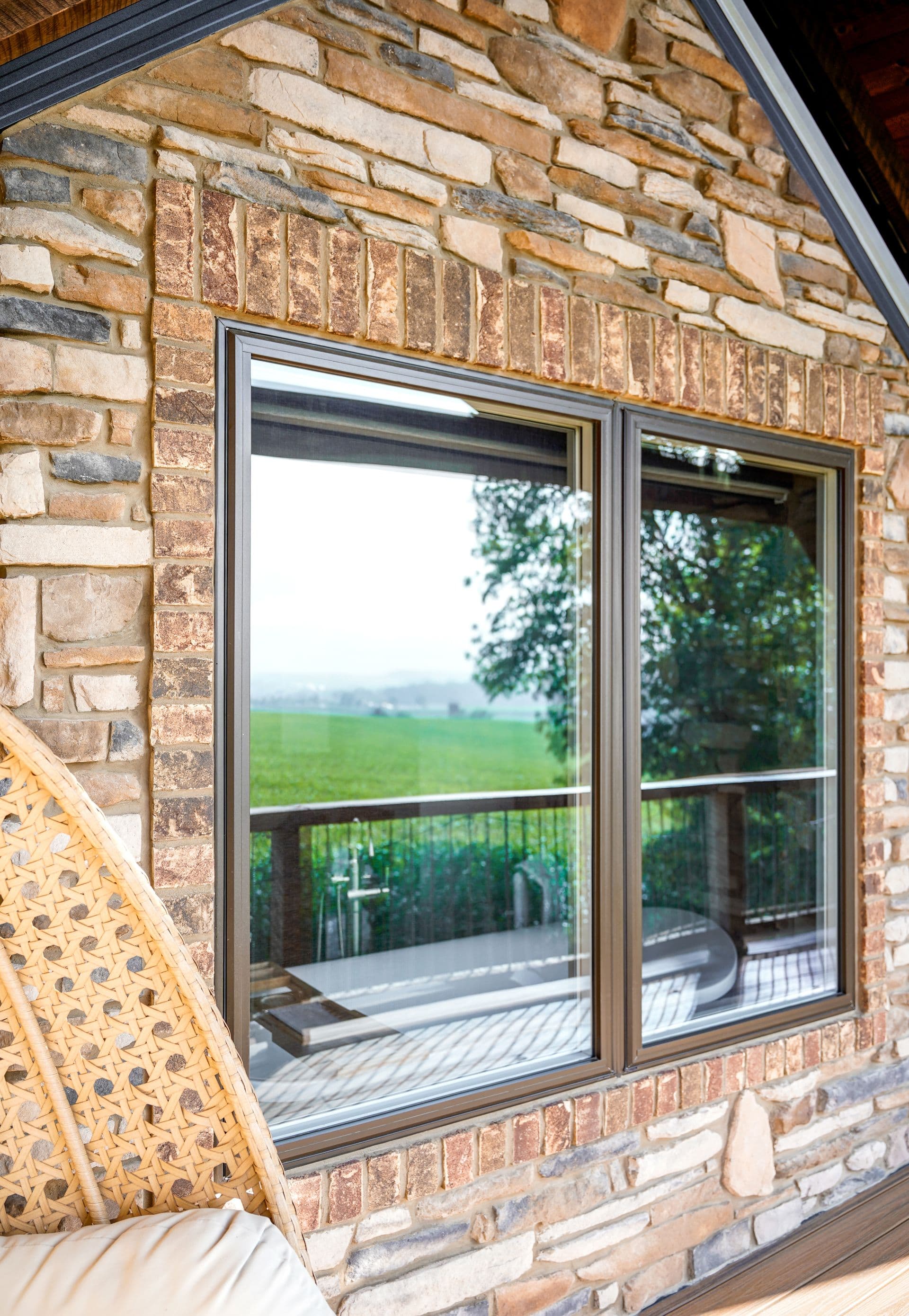 A close-up of a stone-clad house window revealing a serene outdoor landscape.