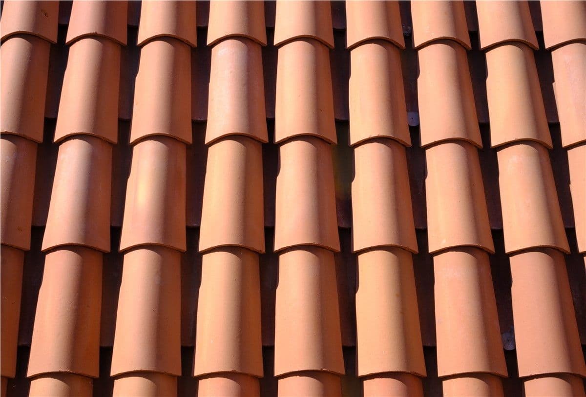 Close-up of overlapping terracotta roof tiles arranged in a repeating pattern under sunlight.
