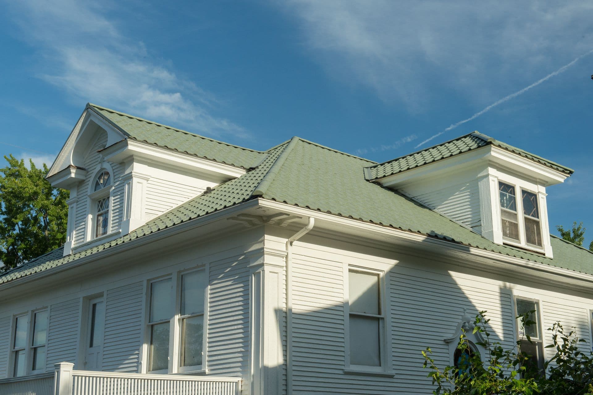 A white clapboard house with a green tiled roof and dormer windows under a blue sky.